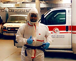 أحد الممارسين الصحيين يرتدي الملابس الواقية من فيروس كورونا أمام سيارة الإسعاف 
